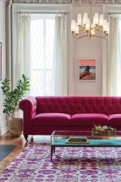 a neutral living room with a magenta sofa, a tiered coffee table, a chandelier, a bold artwork and a potted plant
