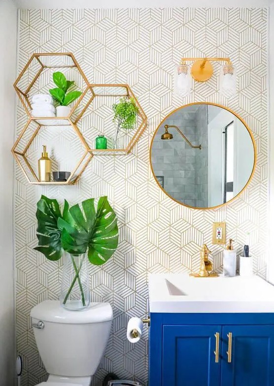 a cool bathroom with printed wallpaper, gold hexagon shelves, a round mirror in a gold frame, gold fixtures and handles is very bold