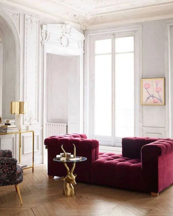 a neutral refined living room with molding on the walls, a magenta sofa, a chic coffee table, a console and a printed chair