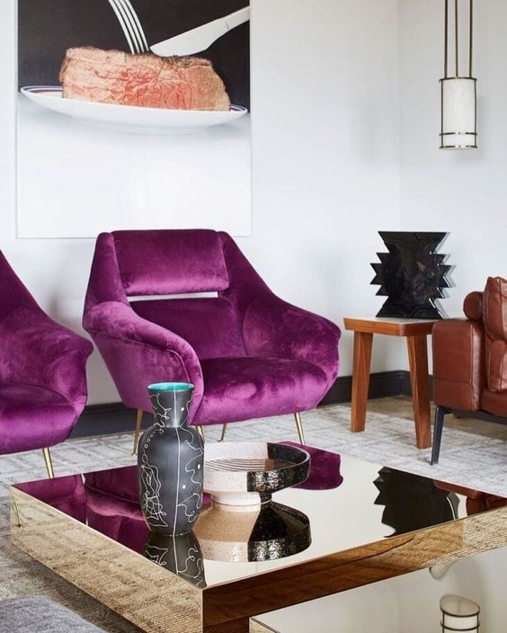 a refined living room with magenta chairs for an accent, a leather sofa and a mirror coffee table plus a pendant lamp