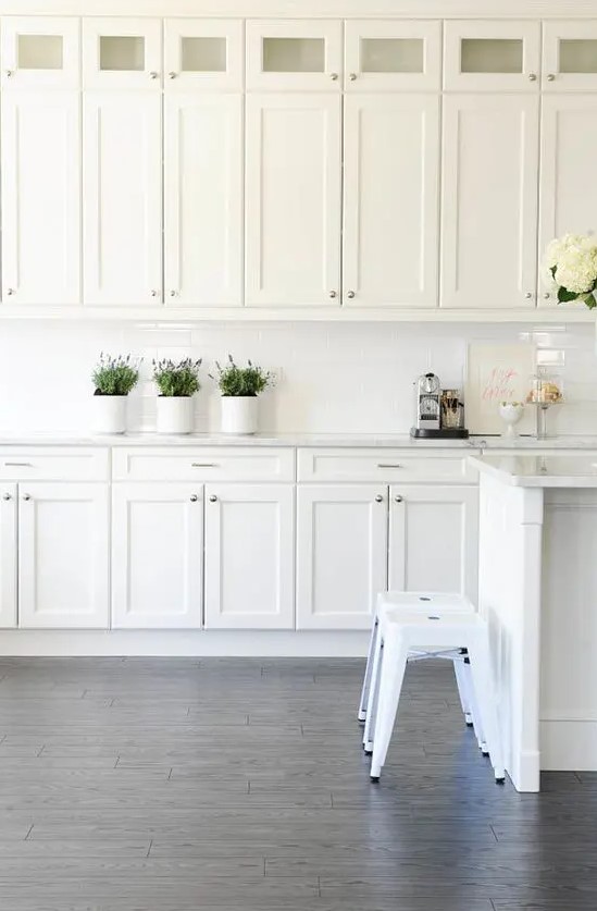 a vintage white kitchen with a white tile backsplash, stools and much storage space