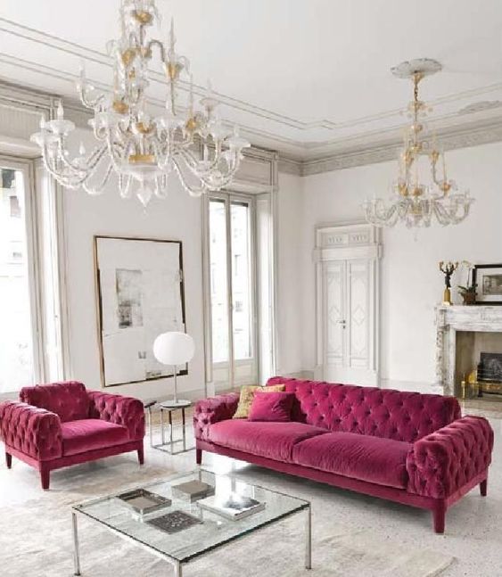 a sophisticated neutral living room with a fireplace, magenta seating furniture, a glass coffee table and crystal chandeliers