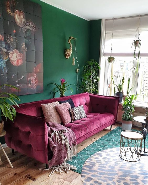 a whimsical living room with a green accent wall, a magenta sofa, a bold floral artwork, layered rugs and potted greenery
