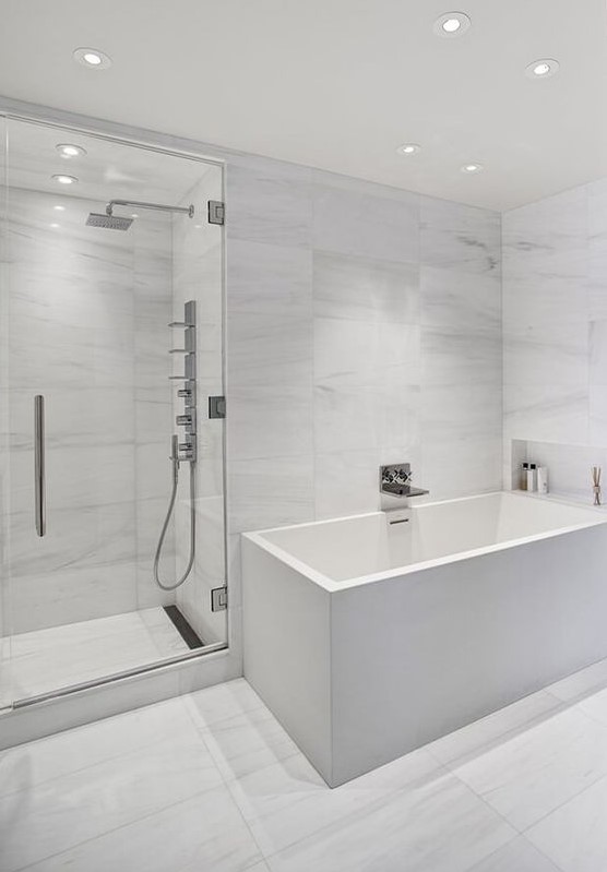 a minimalist white bathroom with marble large scale tiles, a square tub and built-in lights all over