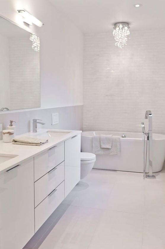 a refined white bathroom clad with tiles of various sizes, with a chic chandelier and a large white vanity