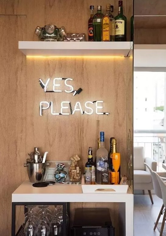 a chic modern home bar with a white bar with open storage, a lit up shelf and a neon sign