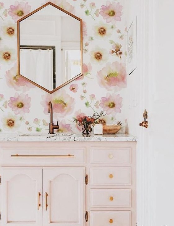 a chic and girlish bathroom with pink floral wallpaper, a light pink vanity and gold and copper fixtures and frames