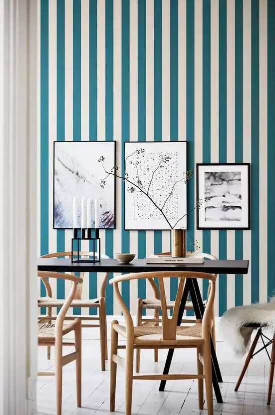 a chic dining room with a blue and white striped wall, a gallery wall, a black table and refined wooden chairs