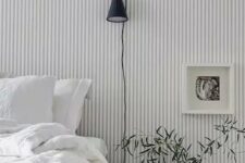 49 a Scandinavian bedroom finished off with a grey and white striped wall, a bed and a nightstand, some greenery and art is welcoming