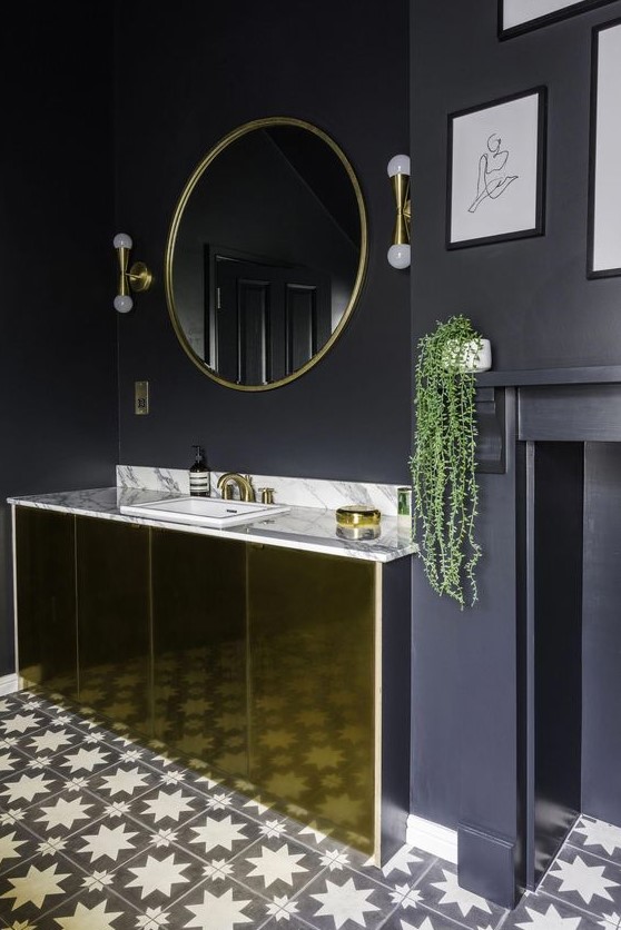 a chic black and gold bathroom with matte black walls, a polished gold vanity, gold fixtures and lamps and a mosaic floor