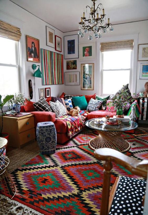 a super colorful and bold boho living room with bright layered rugs, a red sofa with colorful pillows and a bold gallery wall