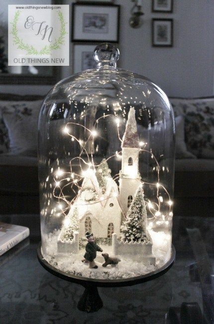 a Christmas cloche terrarium with a snowy scene with a church, a man and a dog and a Christmas tree plus lights