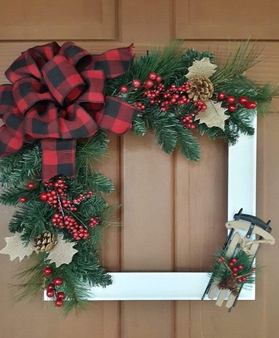 a Christmas frame wreath in white, with evergreens, red berries, pinecones and burlap leaves, a large red bow and a sledge