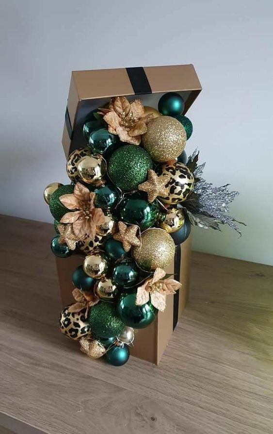 a Christmas gift box with lots of emerald and gold ornaments, faux blooms and stars plus silver branches