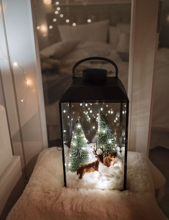 a Christmas lantern terrarium with faux snow, a deer and a bear, bottle brush trees and lights is a very cozy idea