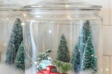 a Christmas terrarium made of a large jar with faux snow, bottle brush trees and a large truck plus lights around