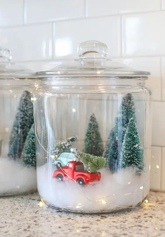 a Christmas terrarium made of a large jar with faux snow, bottle brush trees and a large truck plus lights around