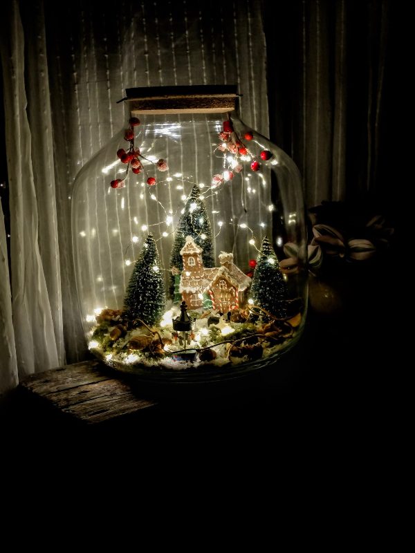 a Christmas terrarium with a gingerbread house, some bottle brush trees, lights and berries, leaves and moss is cool