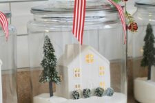 a Christmas terrarium with faux snow, a mini house, a Christmas tree and bushes topped with mini red bells