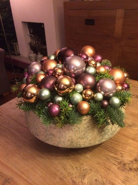 a bowl with a whole arrangement of metallic and pink ornaments and evergreens is a cool holiday centerpiece