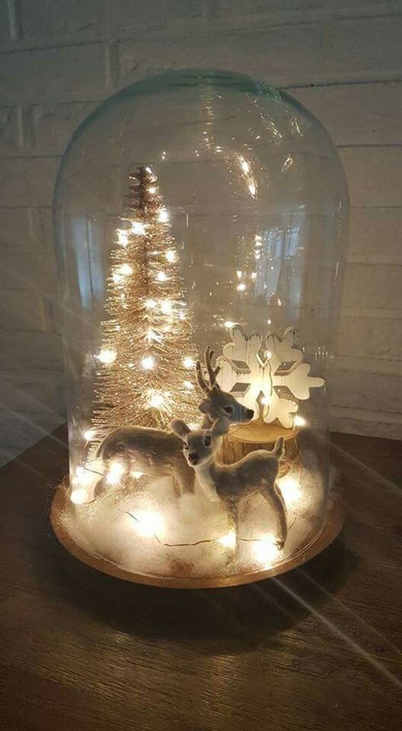 a cloche Christmas terrarium with faux snow, a couple of deer, a snowflake and a bottle brush tree plus lights