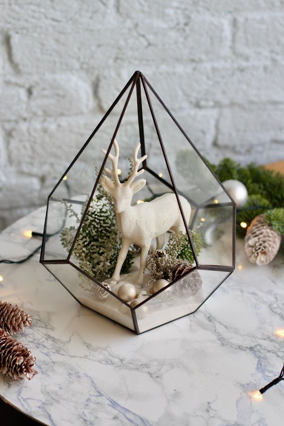 a cool and stylish Christmas terrarium with small ornaments, pinecones, moss and greenery and a white deer