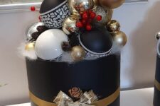 a creative Christmas ornament display as a black rounded box, white, black and gold ornaments, faux snow and some berries