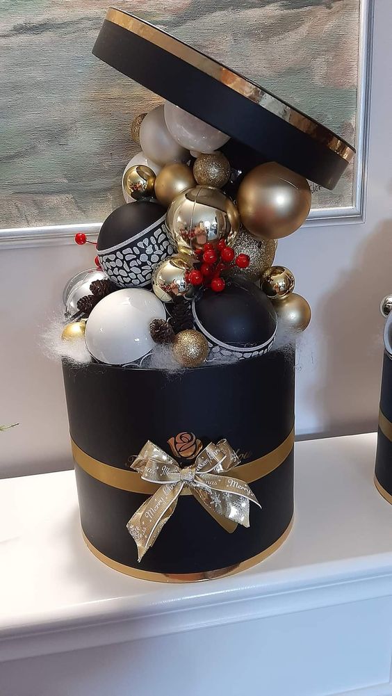 a creative Christmas ornament display as a black rounded box, white, black and gold ornaments, faux snow and some berries