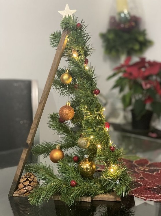 a frame Christmas tree covered with evergreens, with gold and copper ornaments, berries, lights, pinecones and a star on top