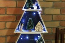 a frame Christmas tree with snowy scenes inside, with lights, trees and some houes and animals is a unique decor idea