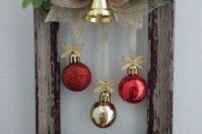 a frame Christmas wreath with greenery, a red and a burlap bow, a gold bell and red and gold ornaments