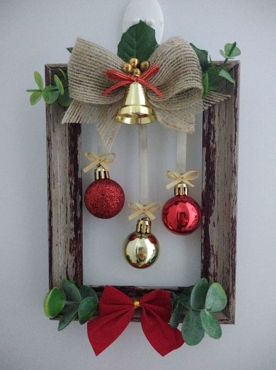 a frame Christmas wreath with greenery, a red and a burlap bow, a gold bell and red and gold ornaments