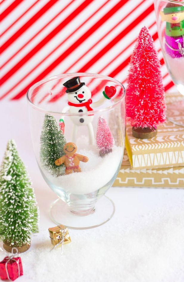 a glass Christmas terrarium with faux snow, a gingerbread man, a snowman, a couple of bottle brush trees