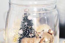 a jar with faux snow, a deer, a Christmas tree and a large ornament is a great example of a Christmas terrarium