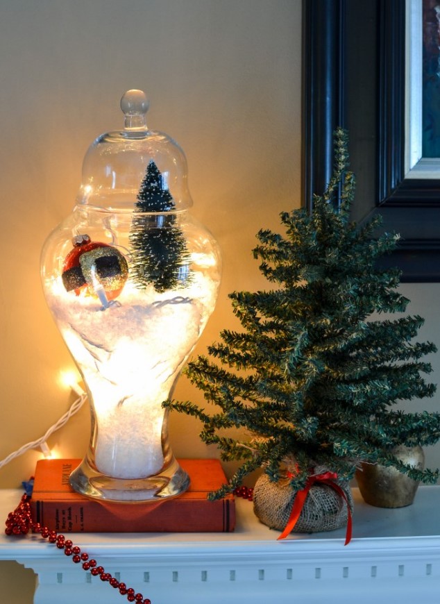 a large jar Christmas terrarium filled with faux snow, with lights, a bottle brush tree and a large Christmas ornament
