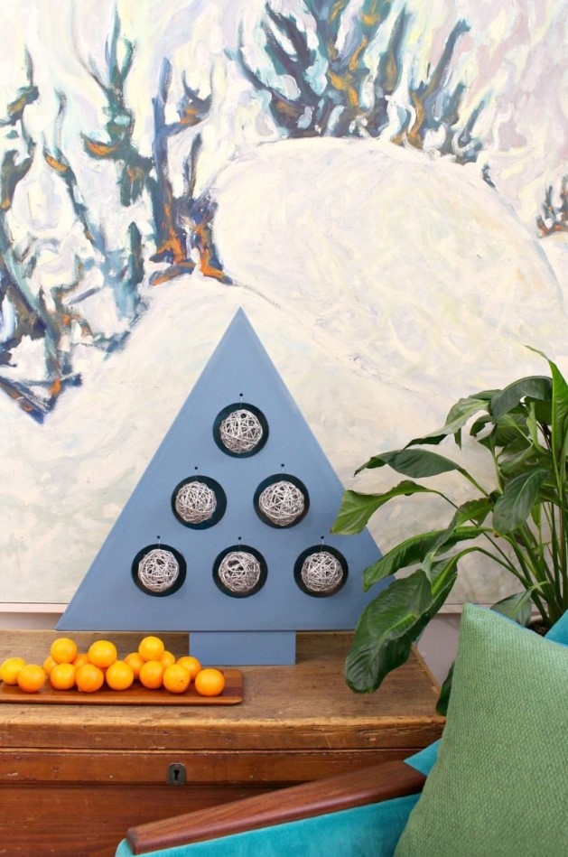 a modern A-framed plywood Christmas tree ornament stand with woven yarn ornaments inside is a creative DIY piece