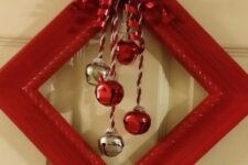 a red frame Christmas wreath with silver and red bells and a bow with leaves and berries is a traditional decor idea for a front door