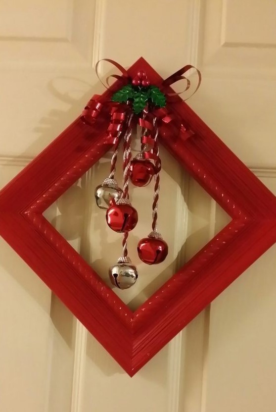a red frame Christmas wreath with silver and red bells and a bow with leaves and berries is a traditional decor idea for a front door