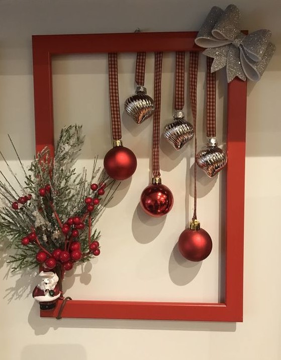a red frame Christmas wreath with silver and red ornaments, a silver glitter bow, evergreens, berries and a Santa Claus