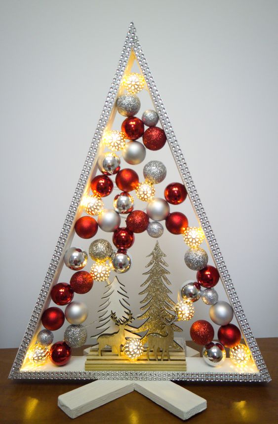 a shiny and glam tabletop Christmas tree with silver, glitter and red ornaments, some glitter trees and deer and lights inside
