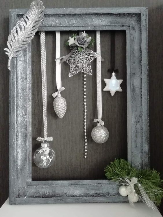 a silver Christmas frame wreath with silver and white ornaments, a star and some beads, a silver feather and evergreens