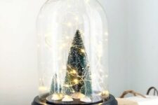 a small and cute Christmas terrarium with bottle brush Christmas trees and lights is a cool decor idea