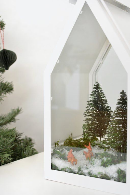 a white Christmas terrarium with faux snow, greenery, bottle brush Christmas trees and tiny deer figurines