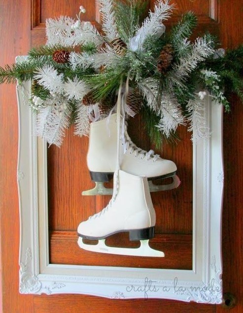 a white frame Christmas wreath with green and white evergreens and pinecones plus some skates hanging down is very creative