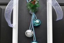 a white picture frame wreath with silver and turquoise bells, evergreens and pinecones and a large sheer bow on top