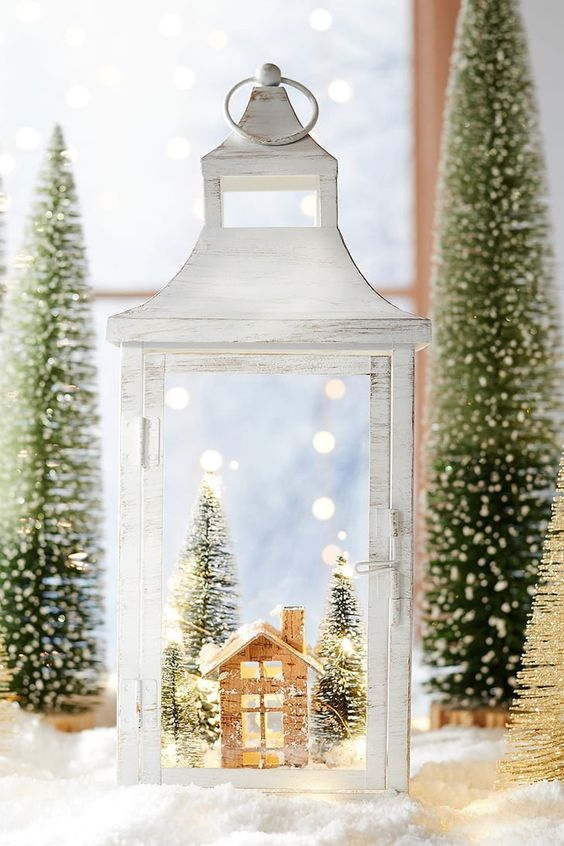 a whitewashed lantern with a snowy scene inside   a little house and bottle brush trees for vintage Christmas decor