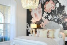 02 a beautiful bedroom with a dark floral accent wall, a grey upholstered bed with neutral bedding, an upholstered pouf and a beaded chandelier