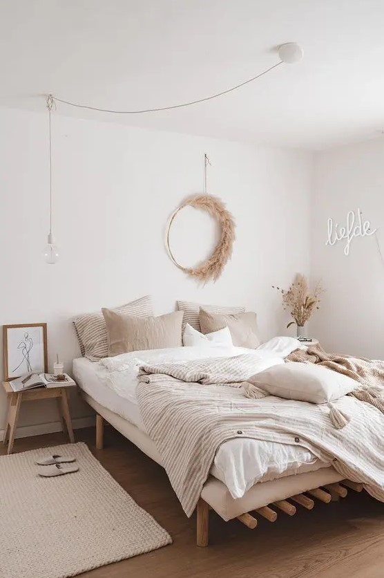 a beautiful modern boho bedroom with wooden furniture, a neon sign, a pampas grass wreath and neutral bedding