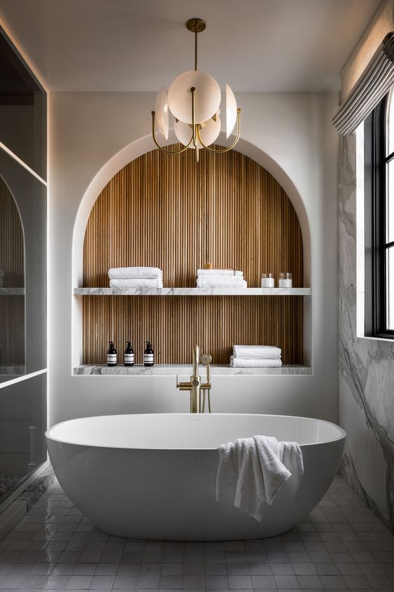 a contemporary to minimalist bathroom with an arched niche with shelves to store some stuff, an oval tub and a chandelier
