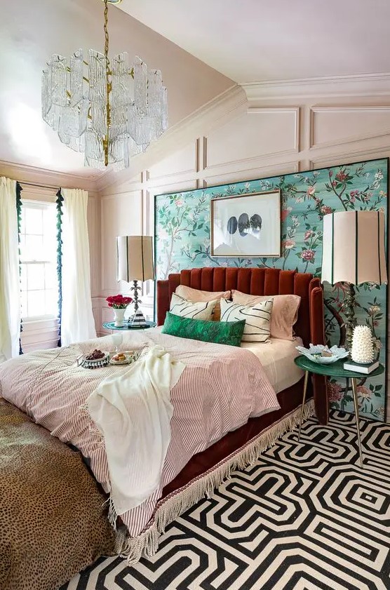 a colorful vintage bedroom with paneling, a bright floral wall, a burgundy bed, colorful bedding and a crystal chandelier